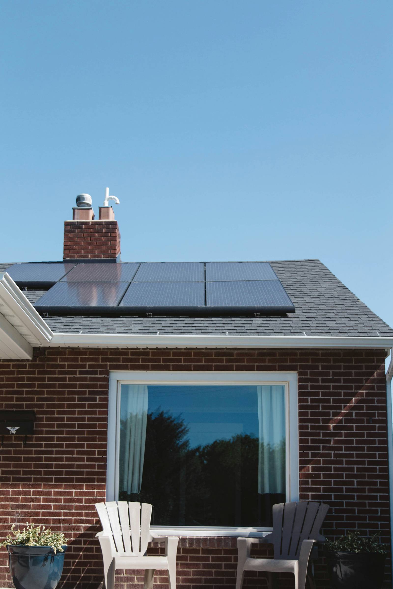 Solar panels on the roof of a brick home, above a large picture window